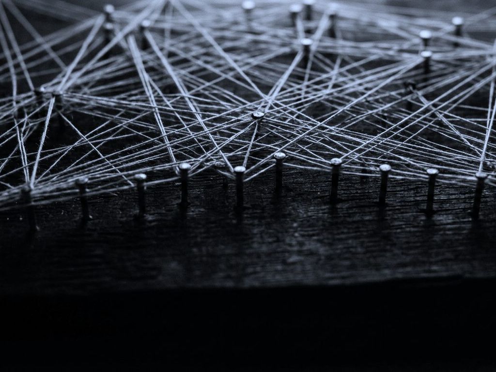 Taut threads stretched between rows of pins on a dark board, forming a dense web.