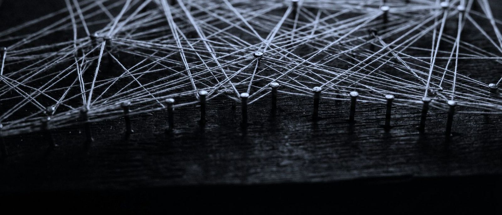 Taut threads stretched between rows of pins on a dark board, forming a dense web.