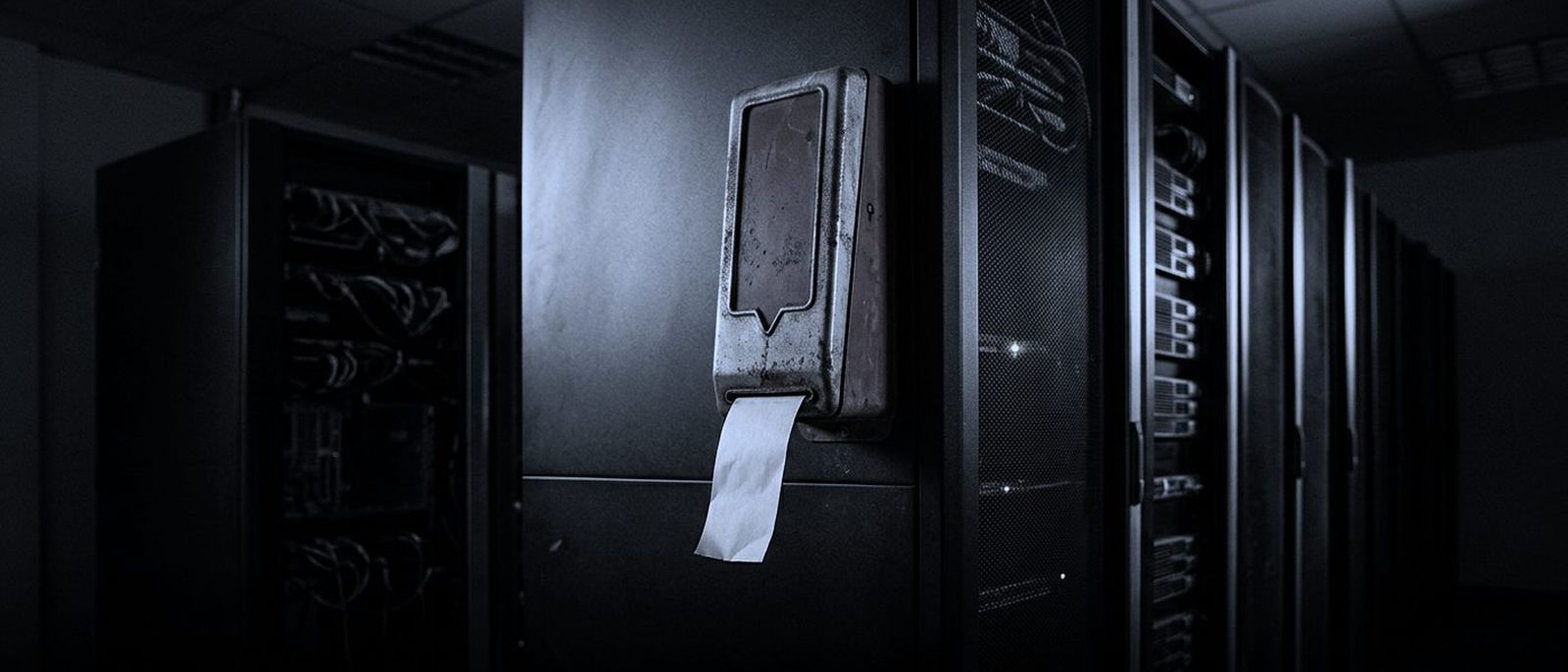 A battered take-a-number ticket dispenser bolted to a server rack in a dark data centre, one blank ticket hanging out.