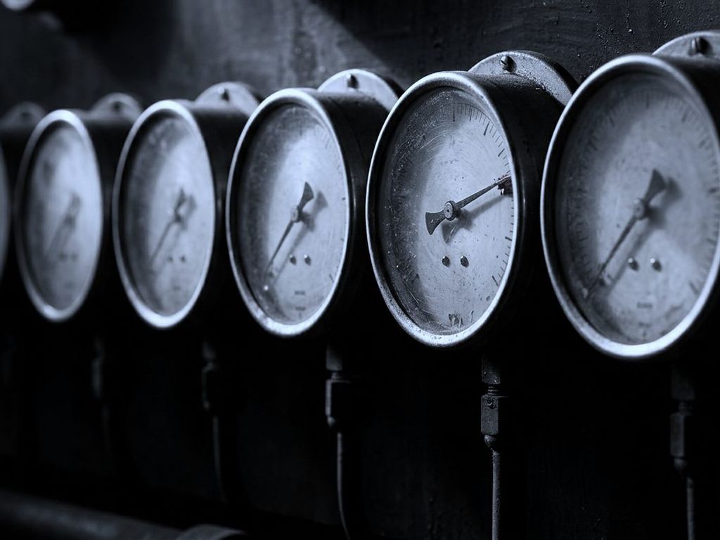A row of round pressure gauges, needles at rest, one pinned hard past its limit.