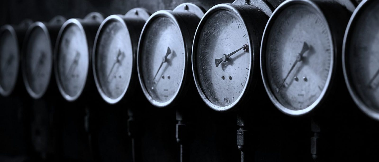 A row of round pressure gauges, needles at rest, one pinned hard past its limit.