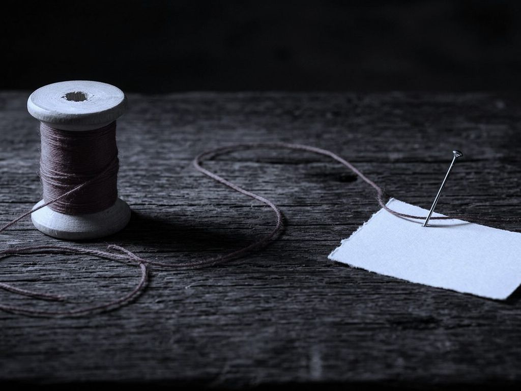 A red thread running across a dark wooden table from a spool to a pinned blank card.