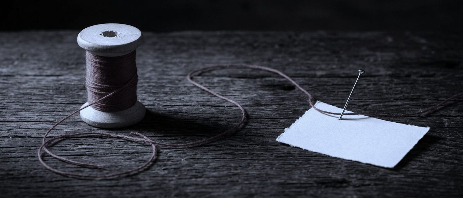 A red thread running across a dark wooden table from a spool to a pinned blank card.