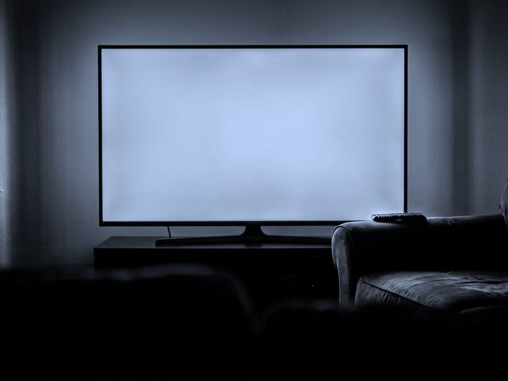 A television glowing in a dark living room, a remote control resting on the sofa arm.