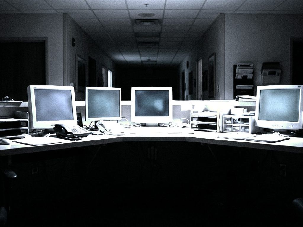 A row of small monitors glowing softly at an empty hospital nurse station at night.