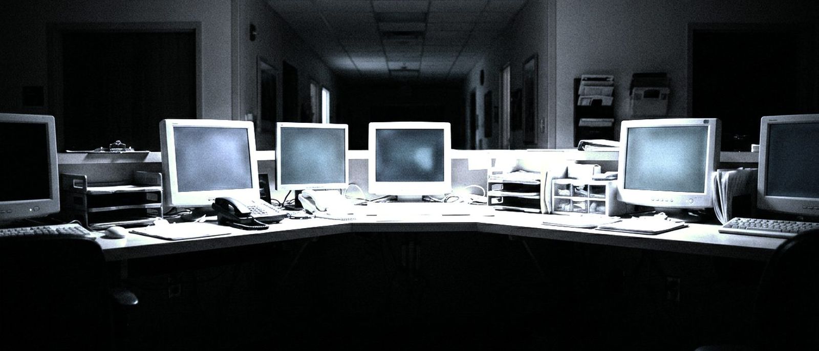 A row of small monitors glowing softly at an empty hospital nurse station at night.