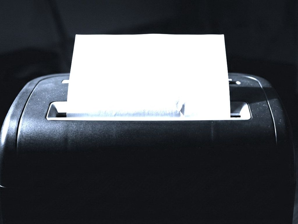A sheet of paper half fed into the slot of a dark office shredder.