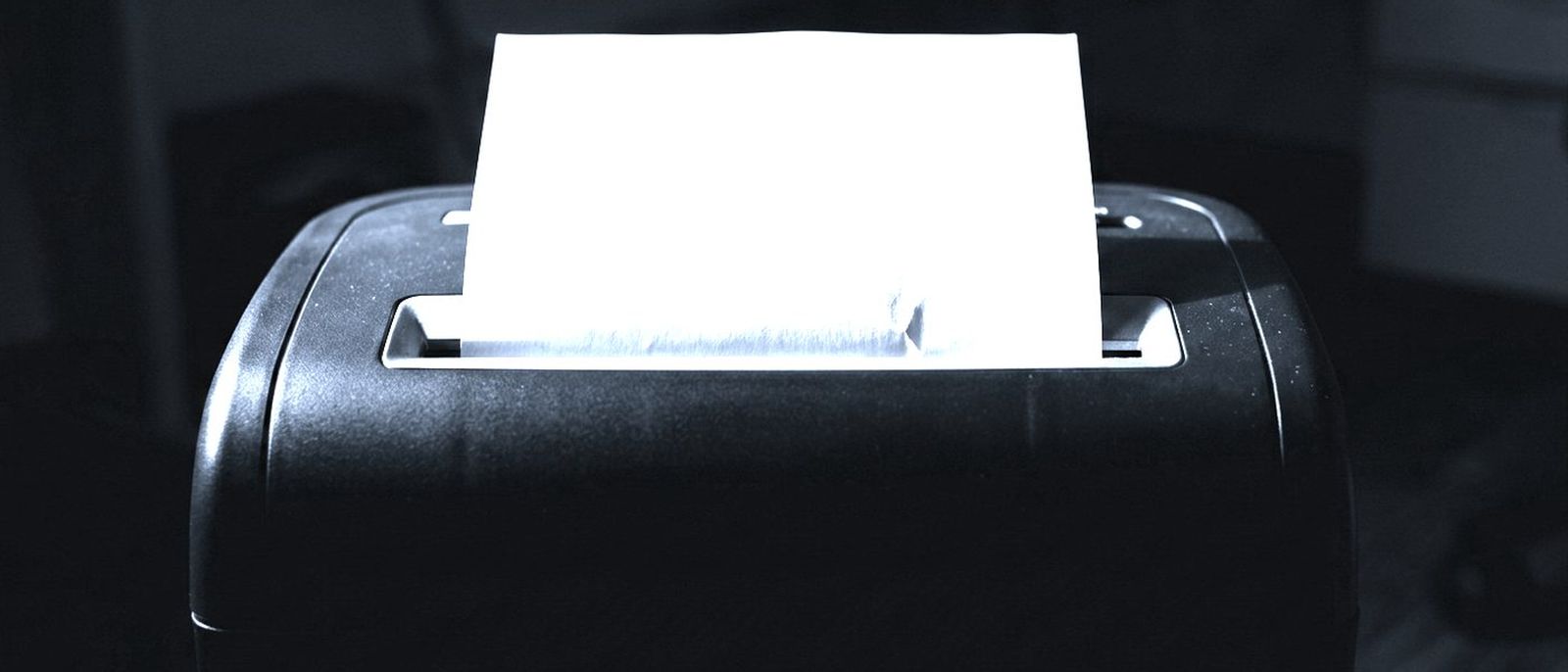 A sheet of paper half fed into the slot of a dark office shredder.