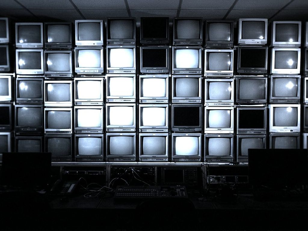 A wall of television screens glowing in a dark broadcast control room.