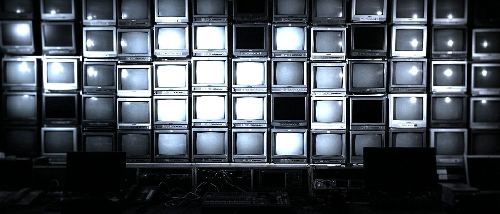 A wall of television screens glowing in a dark broadcast control room.