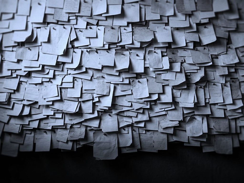 A wall covered with thousands of small paper slips, pinned in dense overlapping rows.