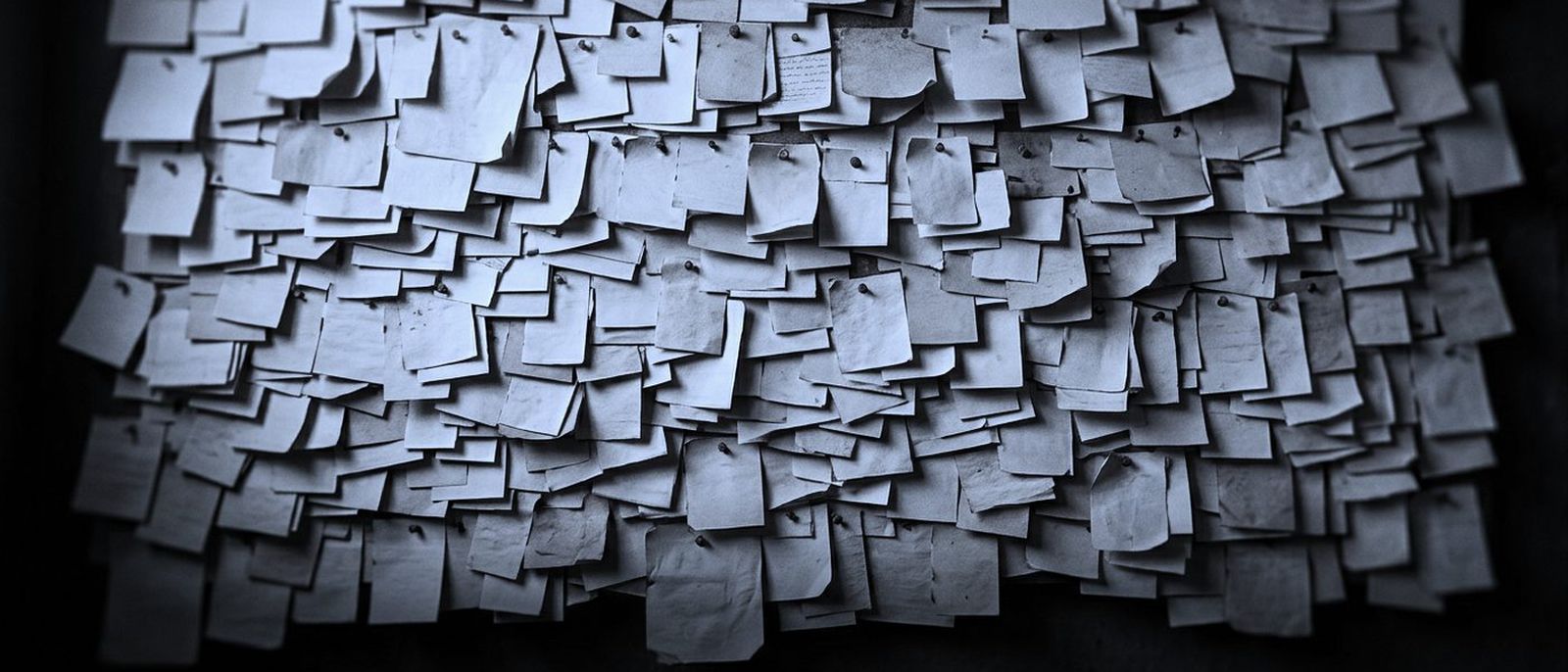 A wall covered with thousands of small paper slips, pinned in dense overlapping rows.