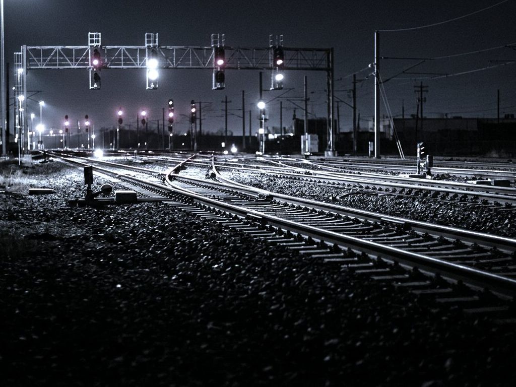 A railway junction at night, several tracks diverging under red and white signal lamps.