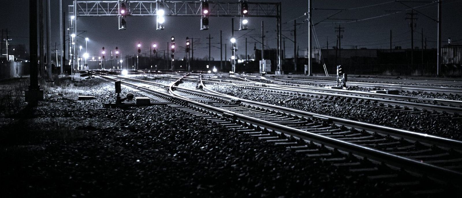 A railway junction at night, several tracks diverging under red and white signal lamps.