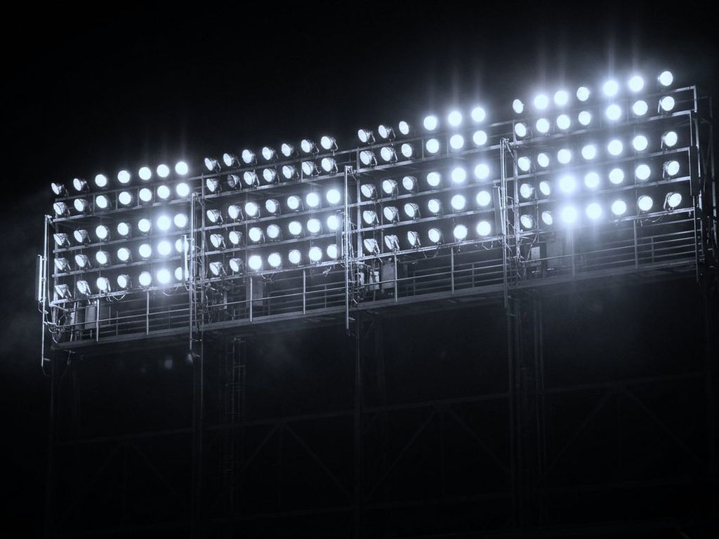 A bank of stadium floodlights at night, rows of lamps in a grid against the dark.
