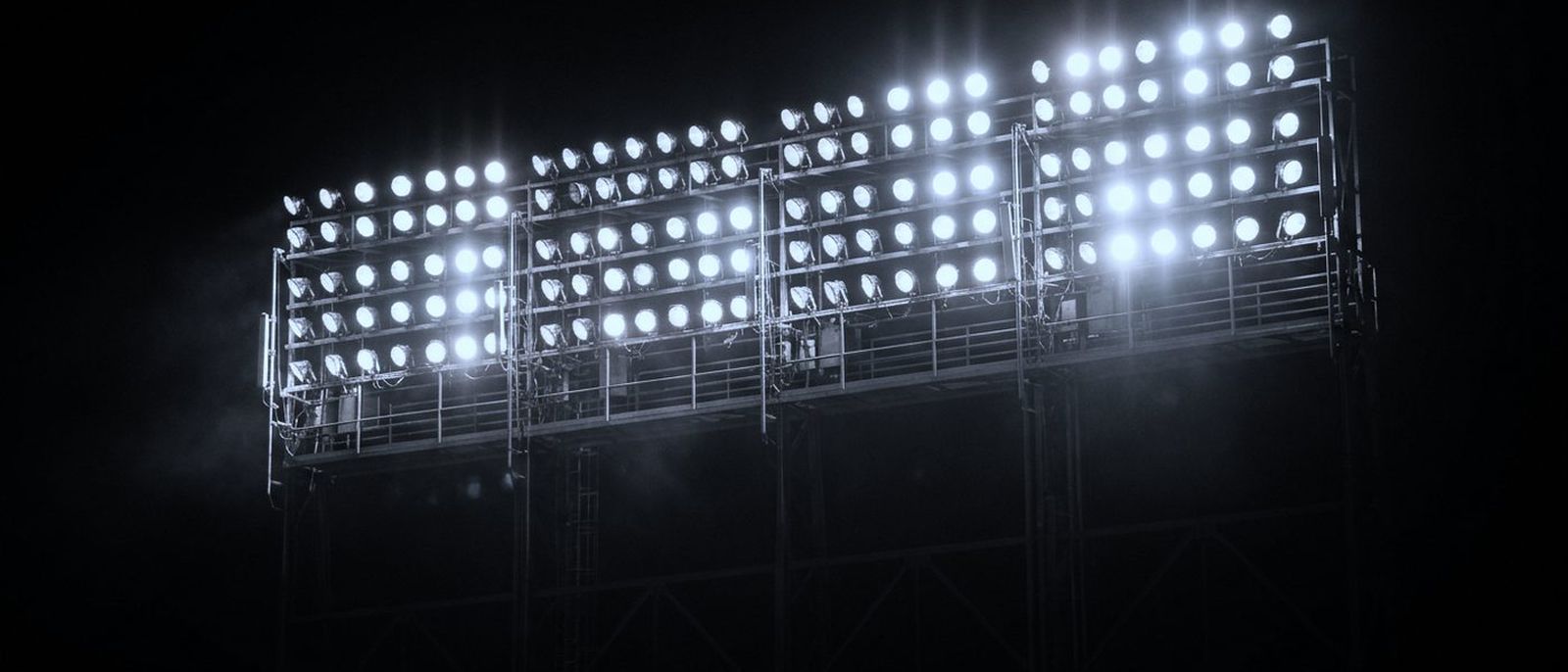 A bank of stadium floodlights at night, rows of lamps in a grid against the dark.