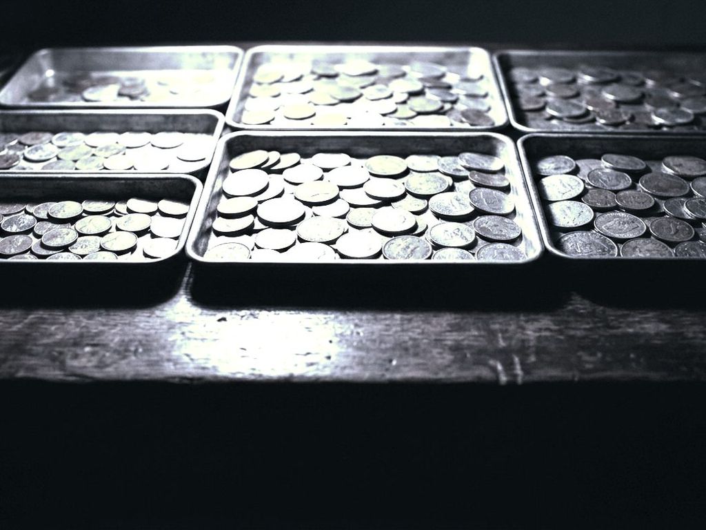 Coins sorted by size into shallow metal trays on a dark desk under one lamp.