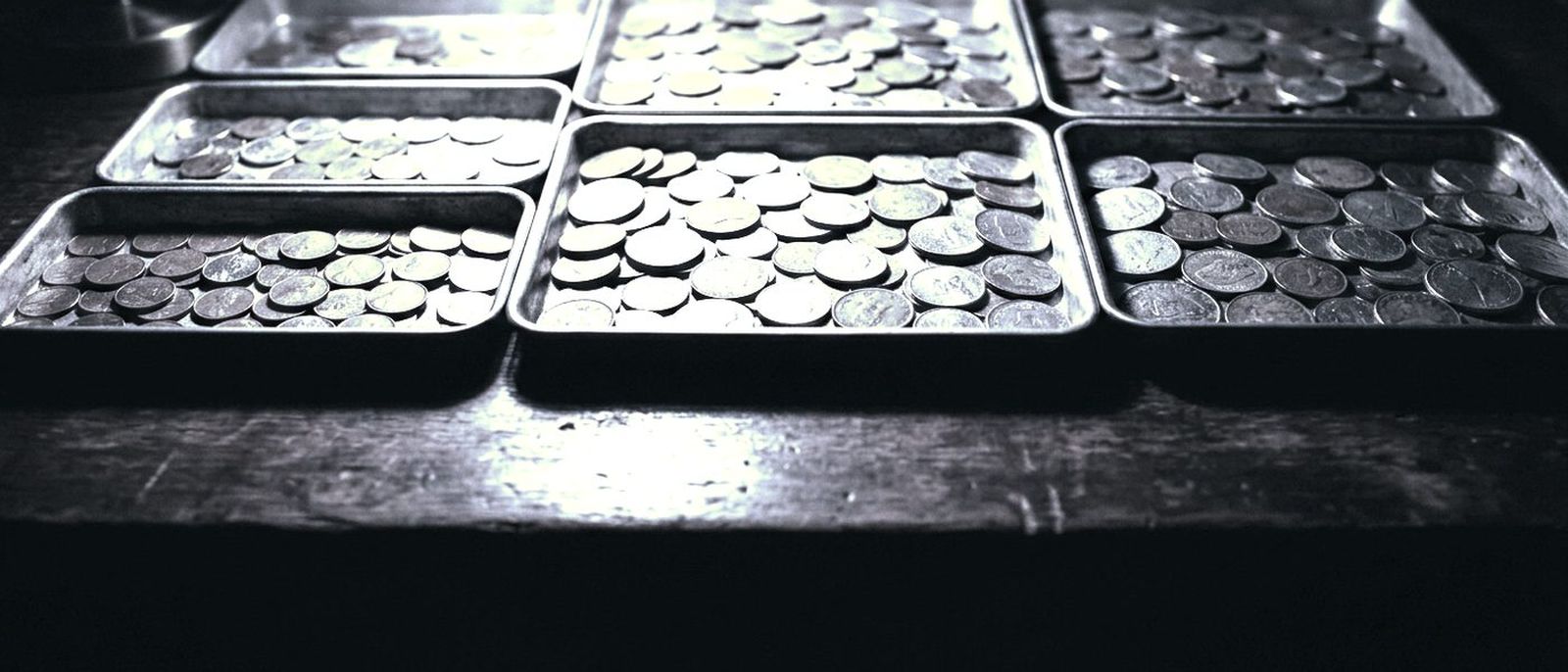 Coins sorted by size into shallow metal trays on a dark desk under one lamp.