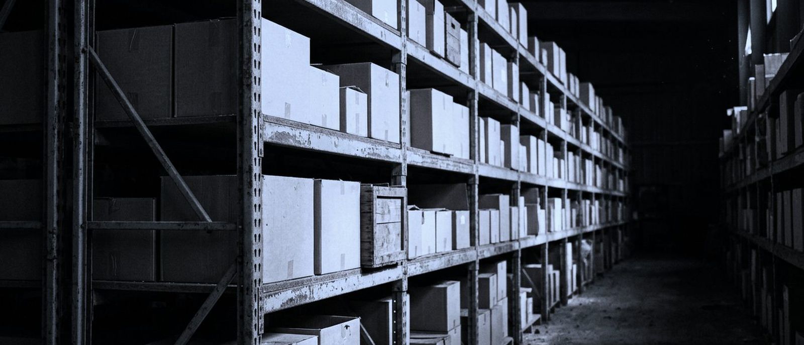 A warehouse aisle receding into the dark, shelving stacked with plain boxes.