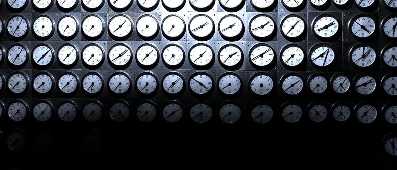A wall of hundreds of small analogue gauges in a dense grid, lit in the centre, needles at different positions.
