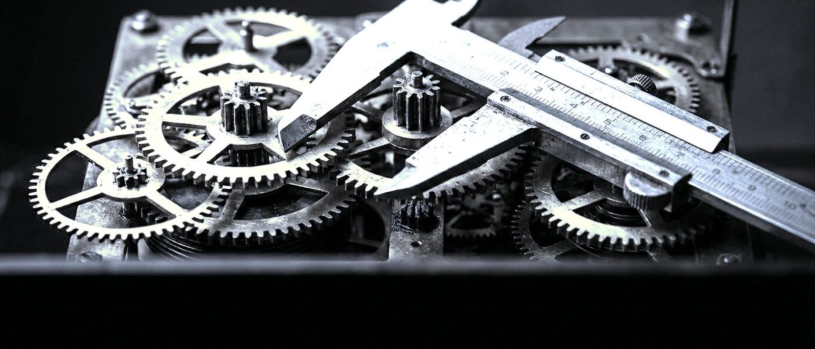 The brass gear train of an old tower clock, a pair of calipers resting across it.