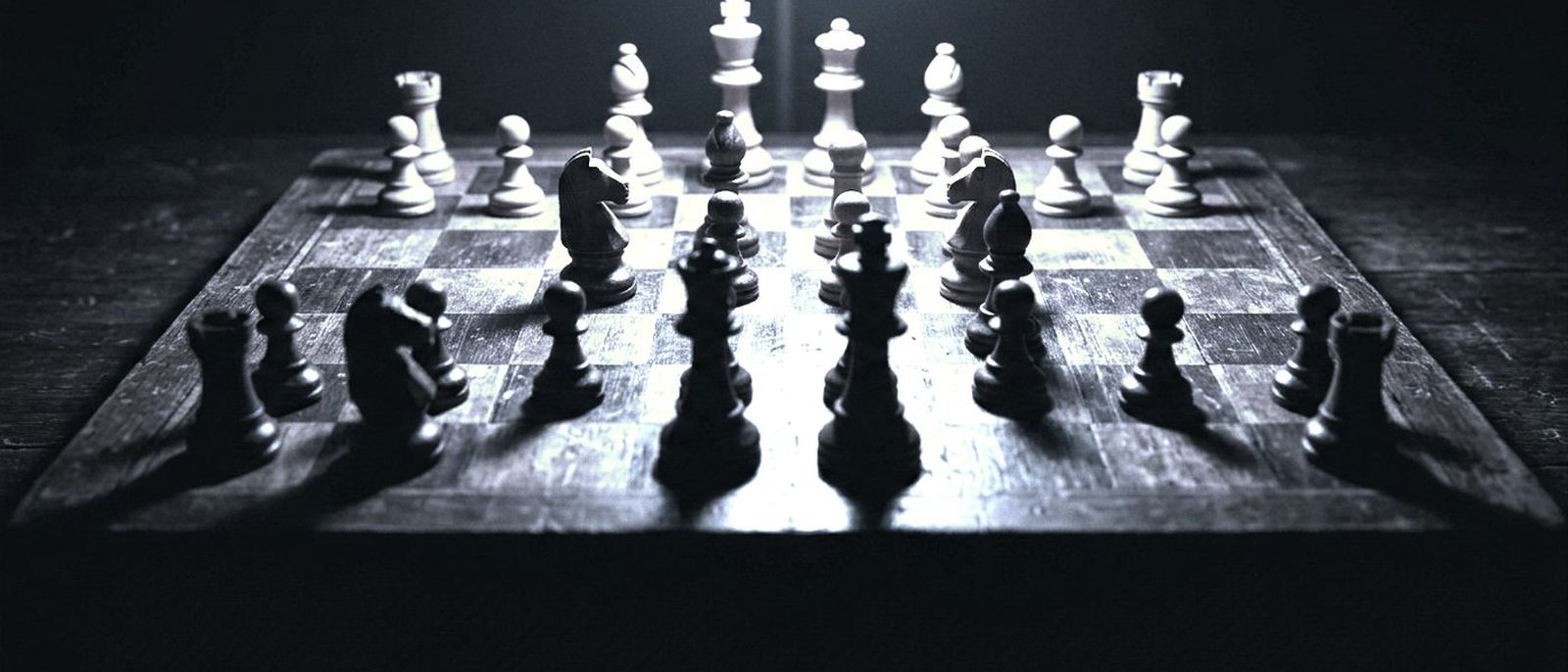 A chess game in progress under a single lamp, the pieces casting long shadows across the board.