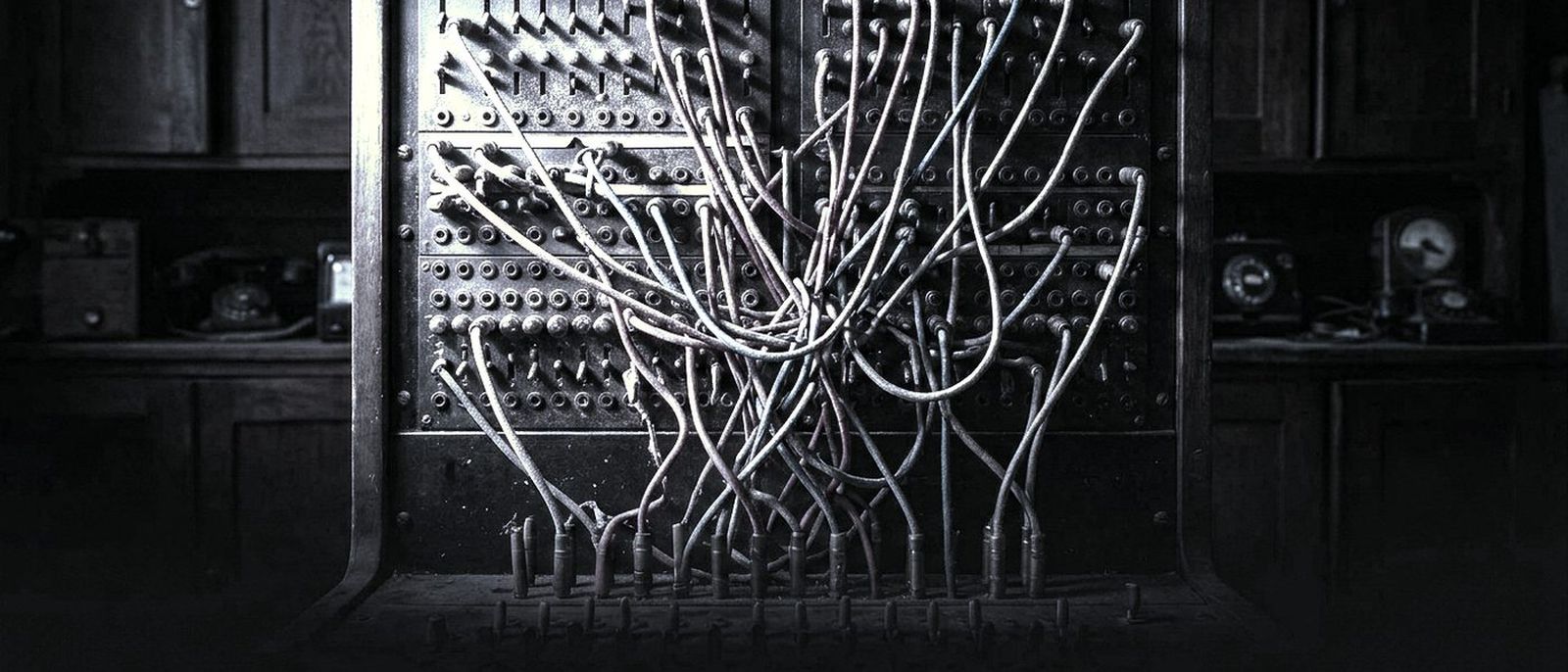 An old telephone switchboard with patch cords plugged across its panel, lit from one side.