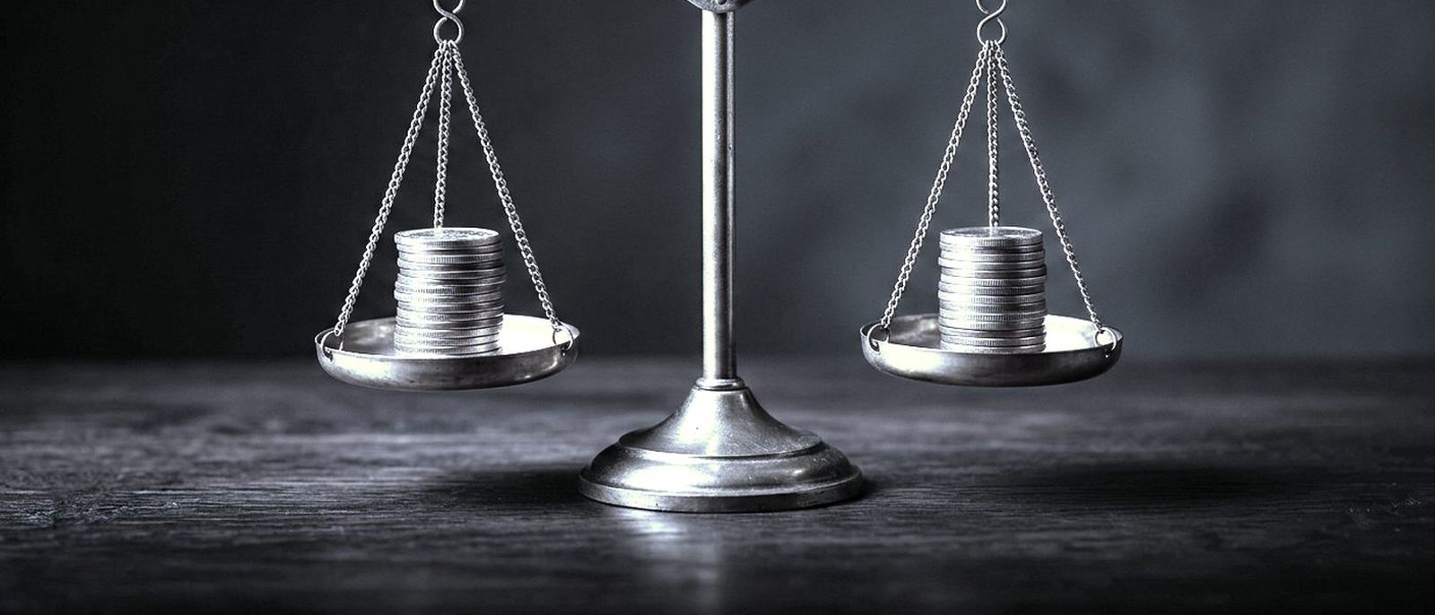 A brass balance scale with neat stacks of coins evenly on both pans, on a dark desk.