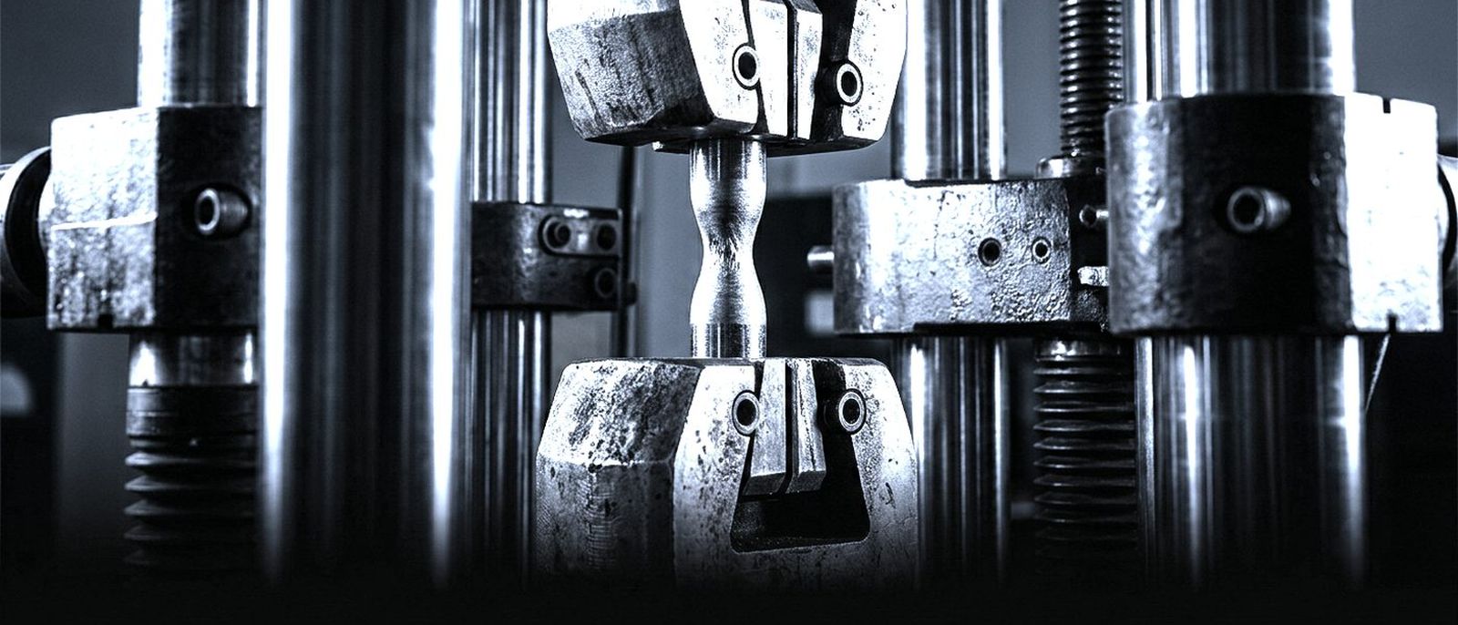 A steel test bar held in the grips of a testing machine, stretched thin at the middle just before it breaks.