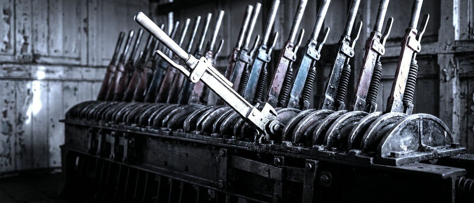 A row of mechanical levers in an old railway signal box, one pulled back from the others.