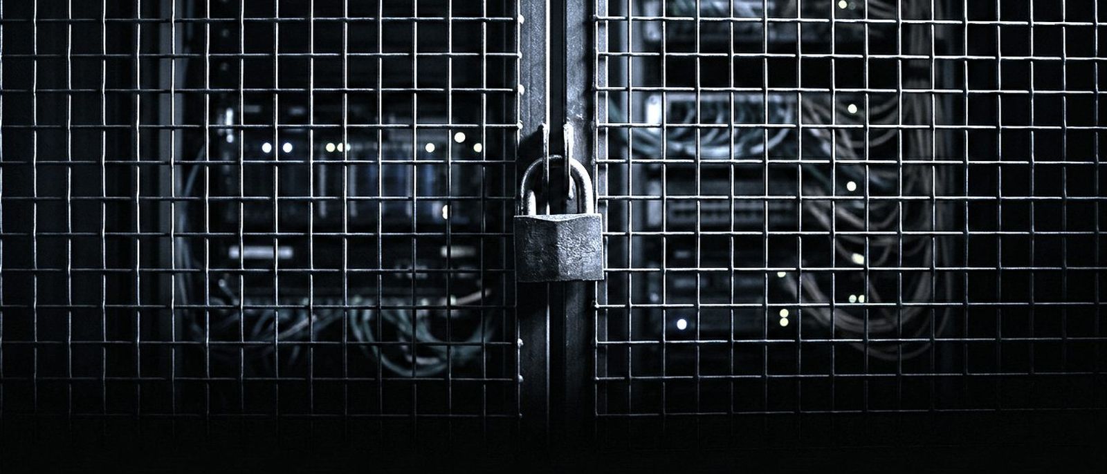 A steel mesh cage door locked with a heavy padlock, server racks glowing faintly behind it.