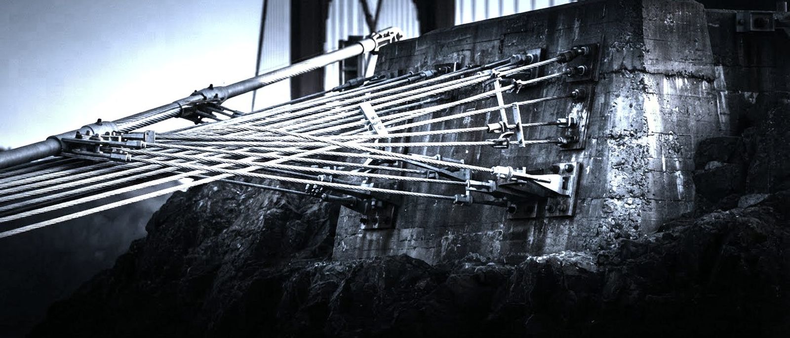 The anchorage of a suspension bridge, steel cable strands fanning out into a massive concrete block.