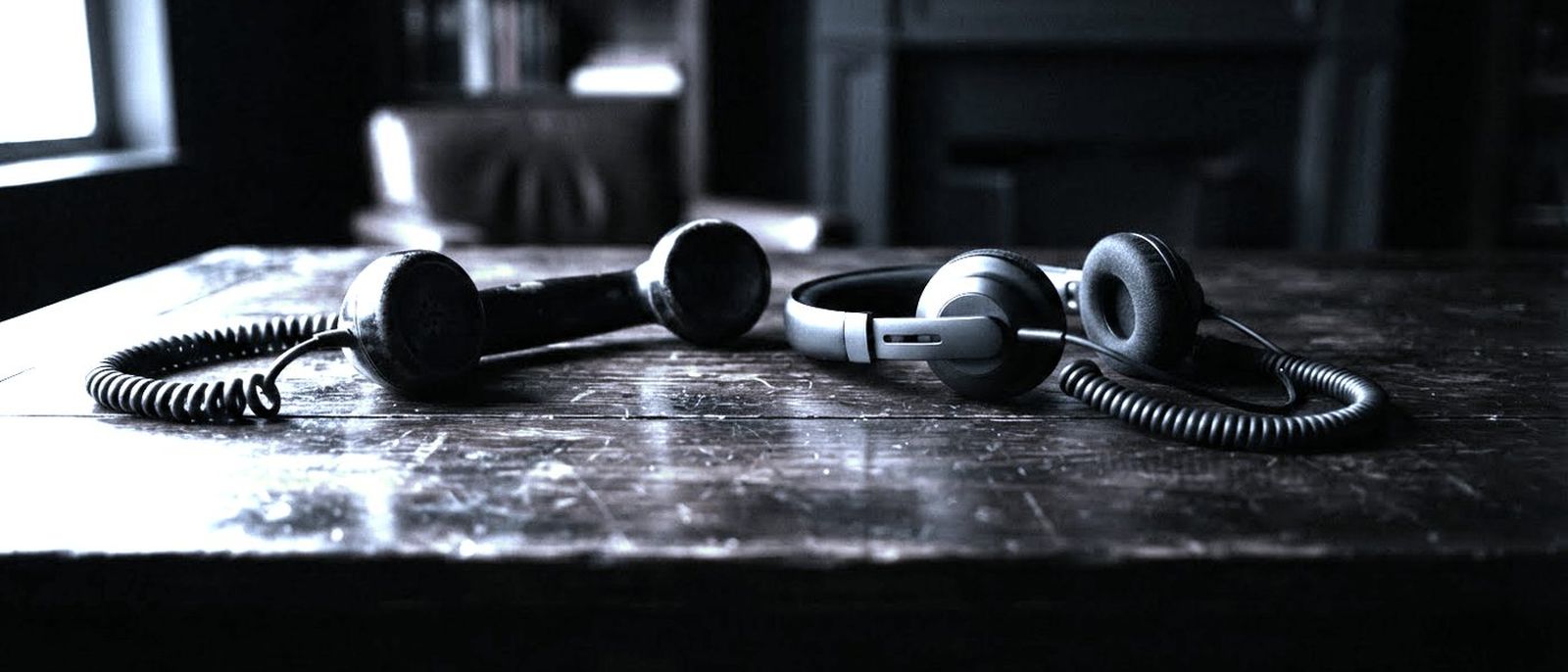 A vintage telephone handset beside a modern headset on a dark wooden desk.