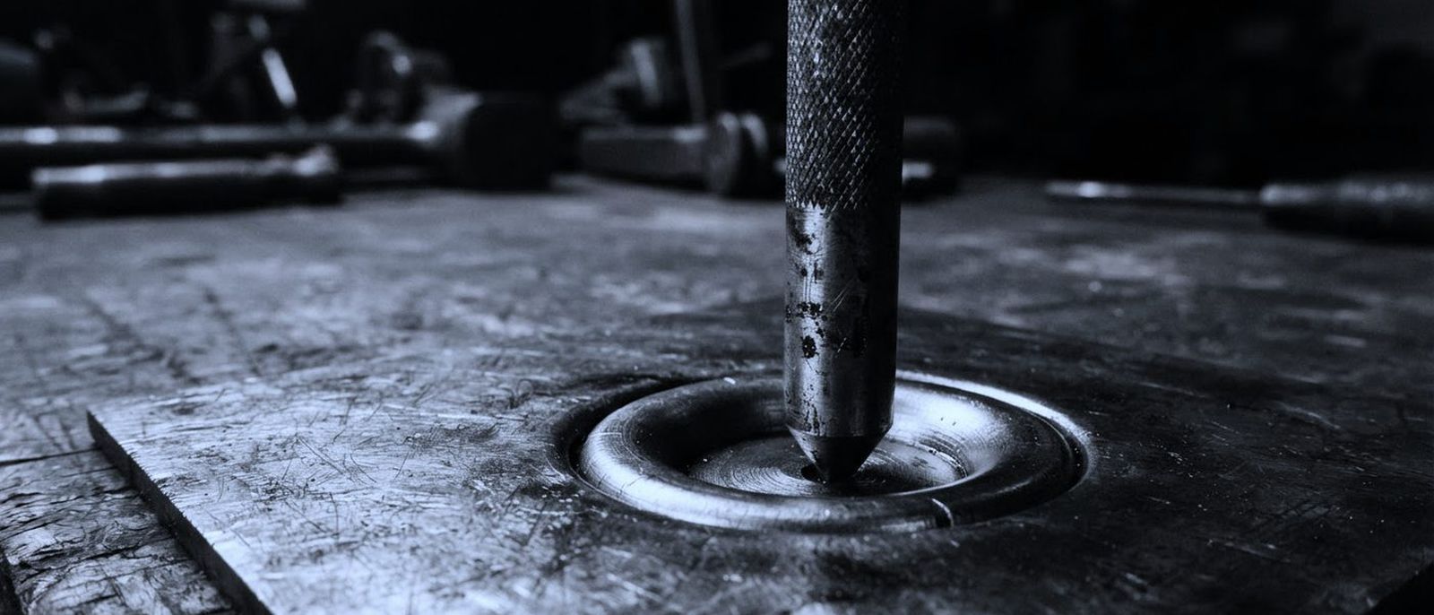 A steel inspection punch standing on a metal plate, its mark struck into the surface.