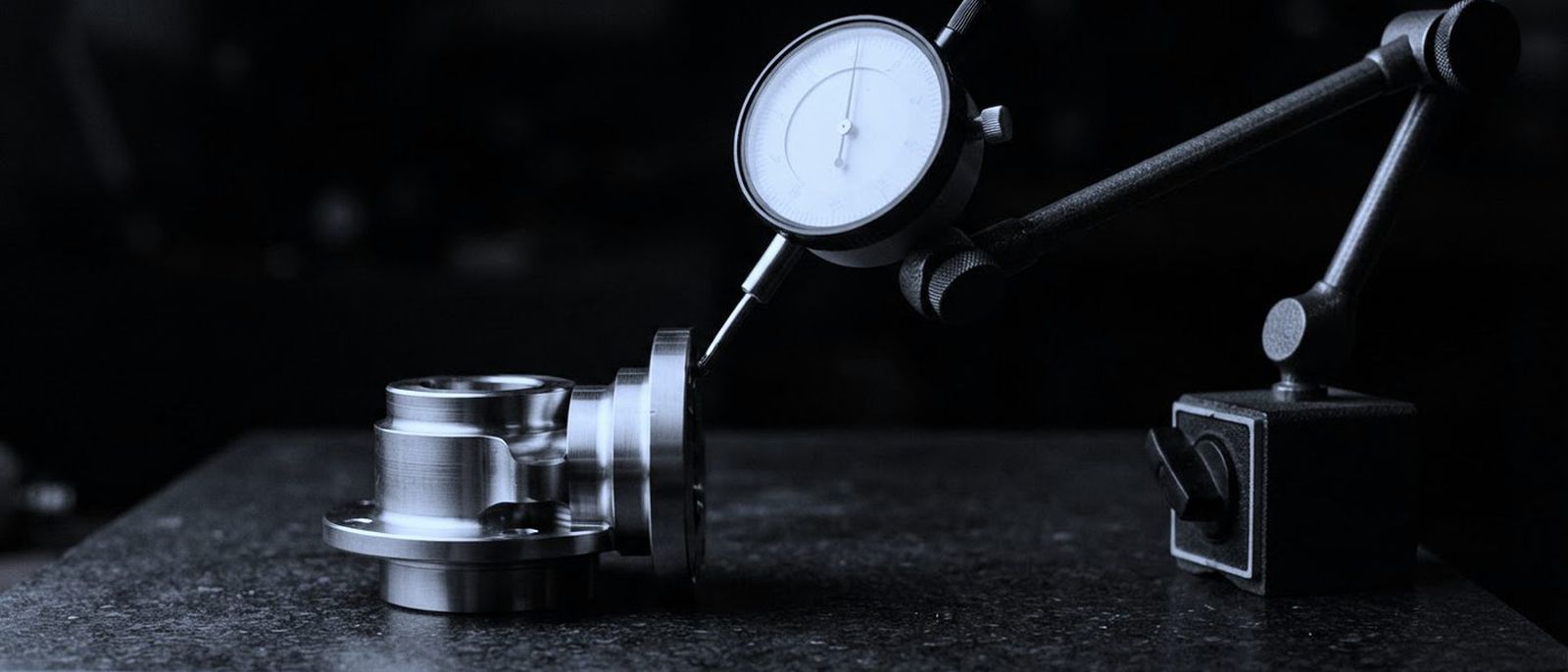 A dial indicator on a magnetic stand, its probe resting against a machined part on a granite surface plate.