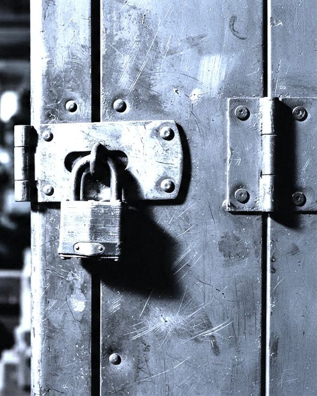 A thick steel hasp and padlock closed on an industrial cabinet door.