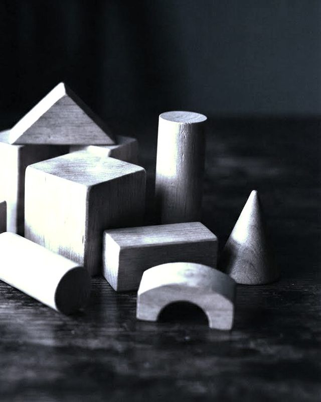 Wooden blocks of different geometric shapes laid out on a dark table, lit from one side.