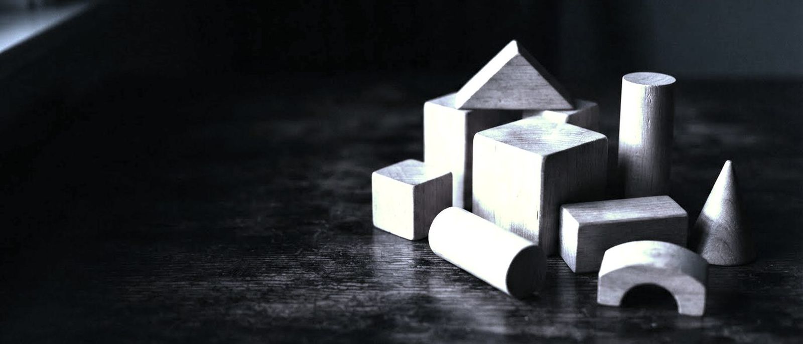 Wooden blocks of different geometric shapes laid out on a dark table, lit from one side.