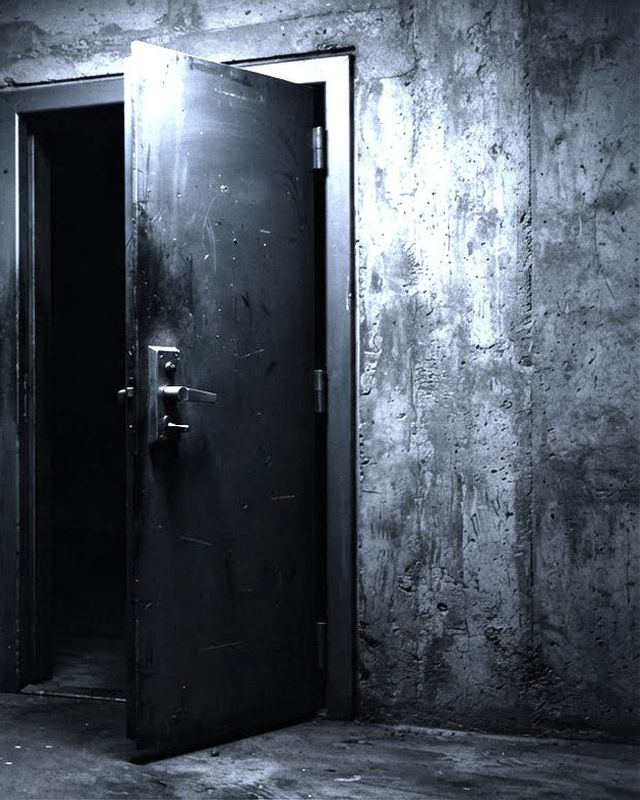 A heavy steel security door with a lever handle, standing slightly open in a concrete wall.