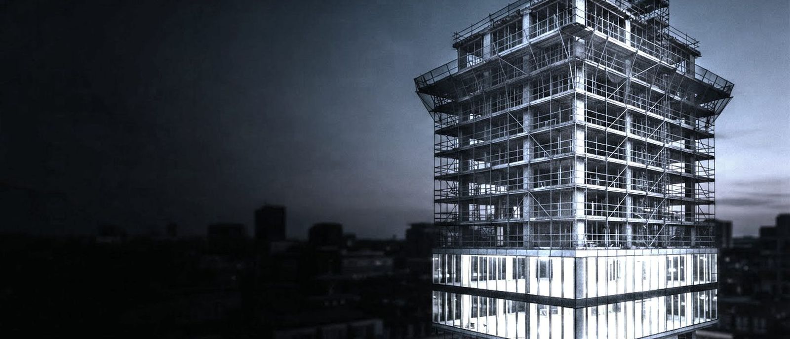 A half-finished concrete building wrapped in scaffolding at dusk, the lower floors glazed and lit.